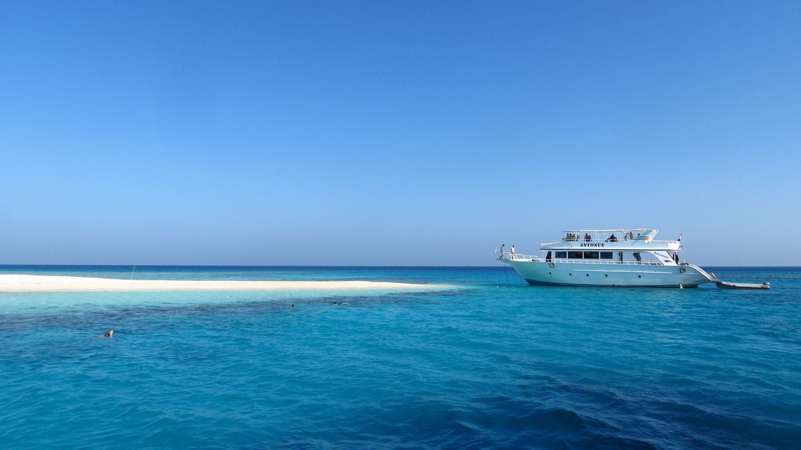 Прогулочная яхта у песчаной косы в Красном море, рядом с ней в бирюзовой воде плавают люди с масками