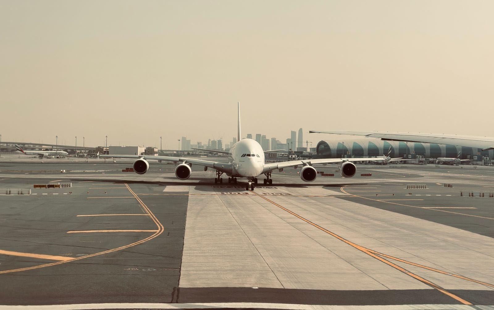 Самолёт Emirates на рулёжной дорожке аэропорта Дубая, за ним терминал и небоскрёбы города
